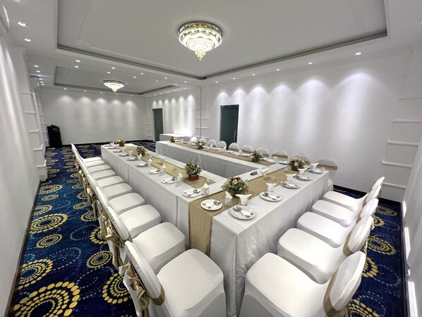 A conference room with a long table set for a formal event, white chairs, and a chandelier.