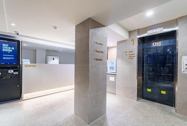A reception area with a self-check-in system, reception desk, and an elevator.