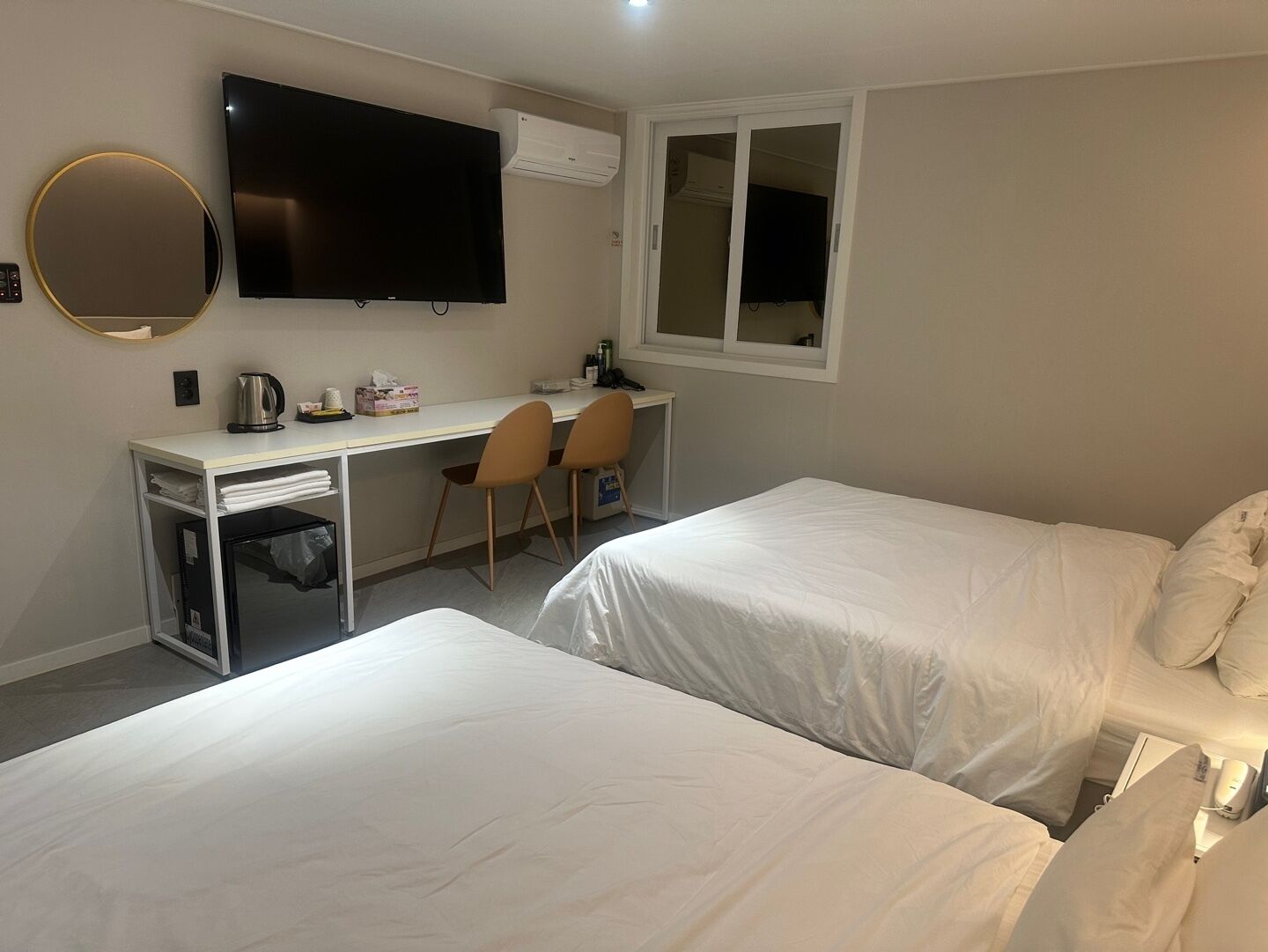A hotel room with a desk, two single beds, a TV, and a window.