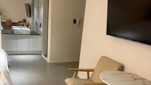 Een moderne hotelkamer met een groot bed, een zithoek met twee stoelen en een tafeltje, een aan de muur bevestigde televisie, en een badkamer zichtbaar door een geopende deur.
