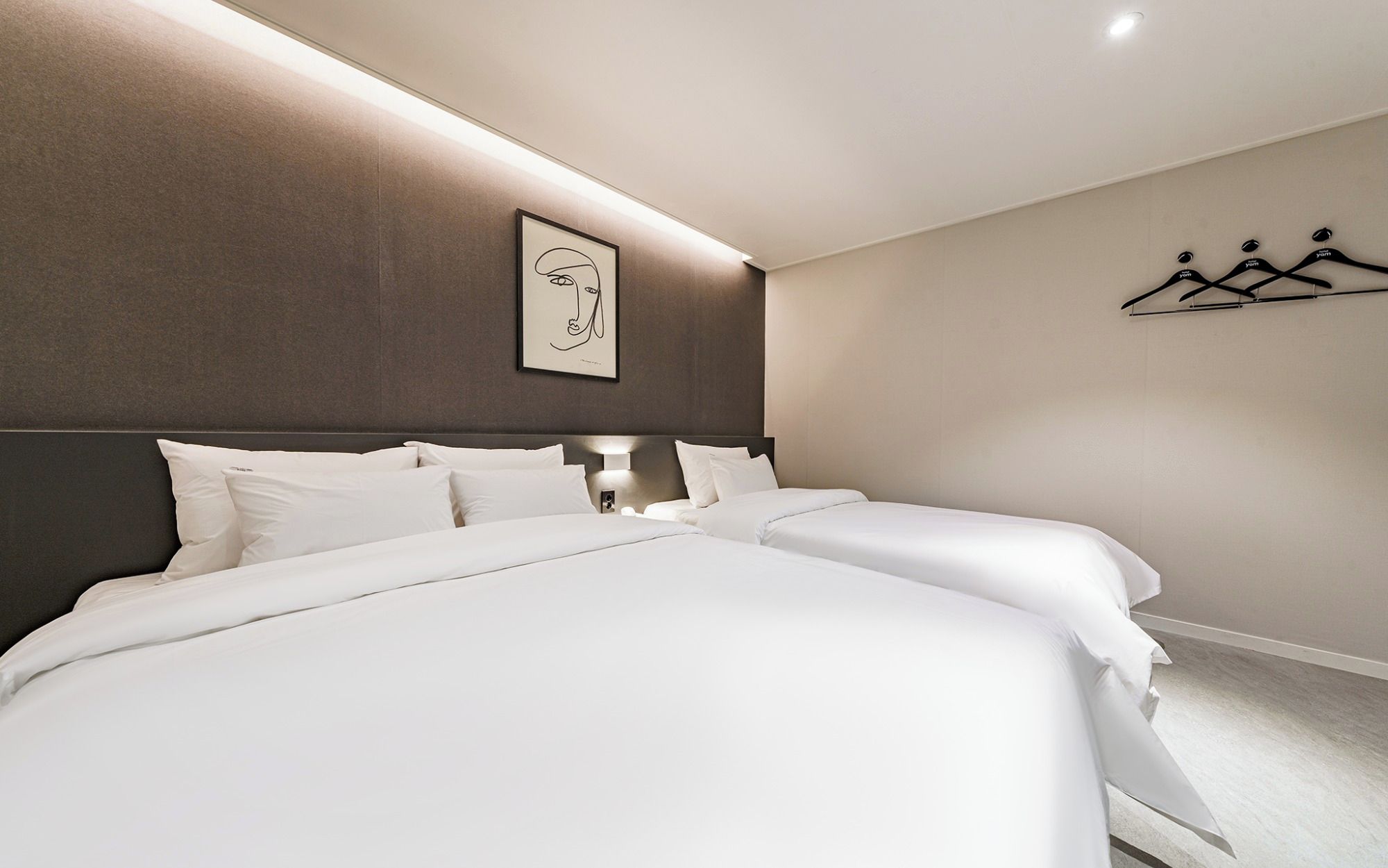 A hotel room with two beds, a headboard, a wall-mounted light, and a coat rack.