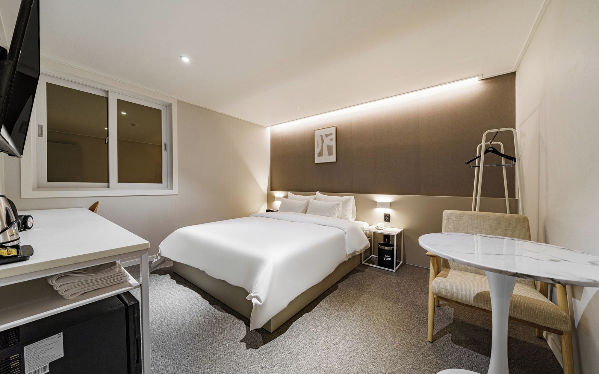 A hotel room with a bed, bedside table, chair, desk, and a television.