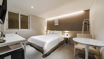 A hotel room with a bed, bedside table, chair, desk, and a television.