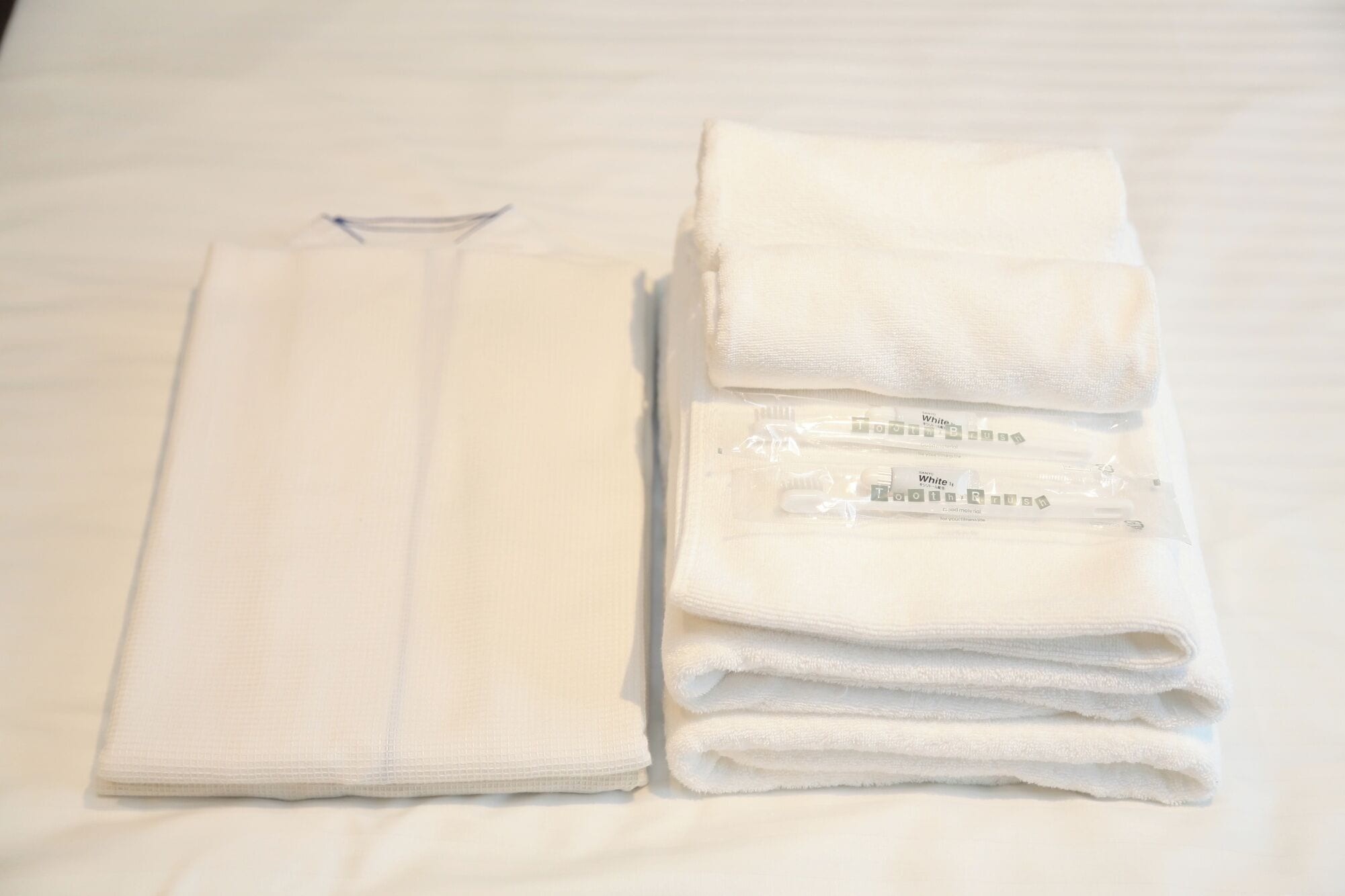 A neatly folded white towel and a set of white bathrobes on a bed.