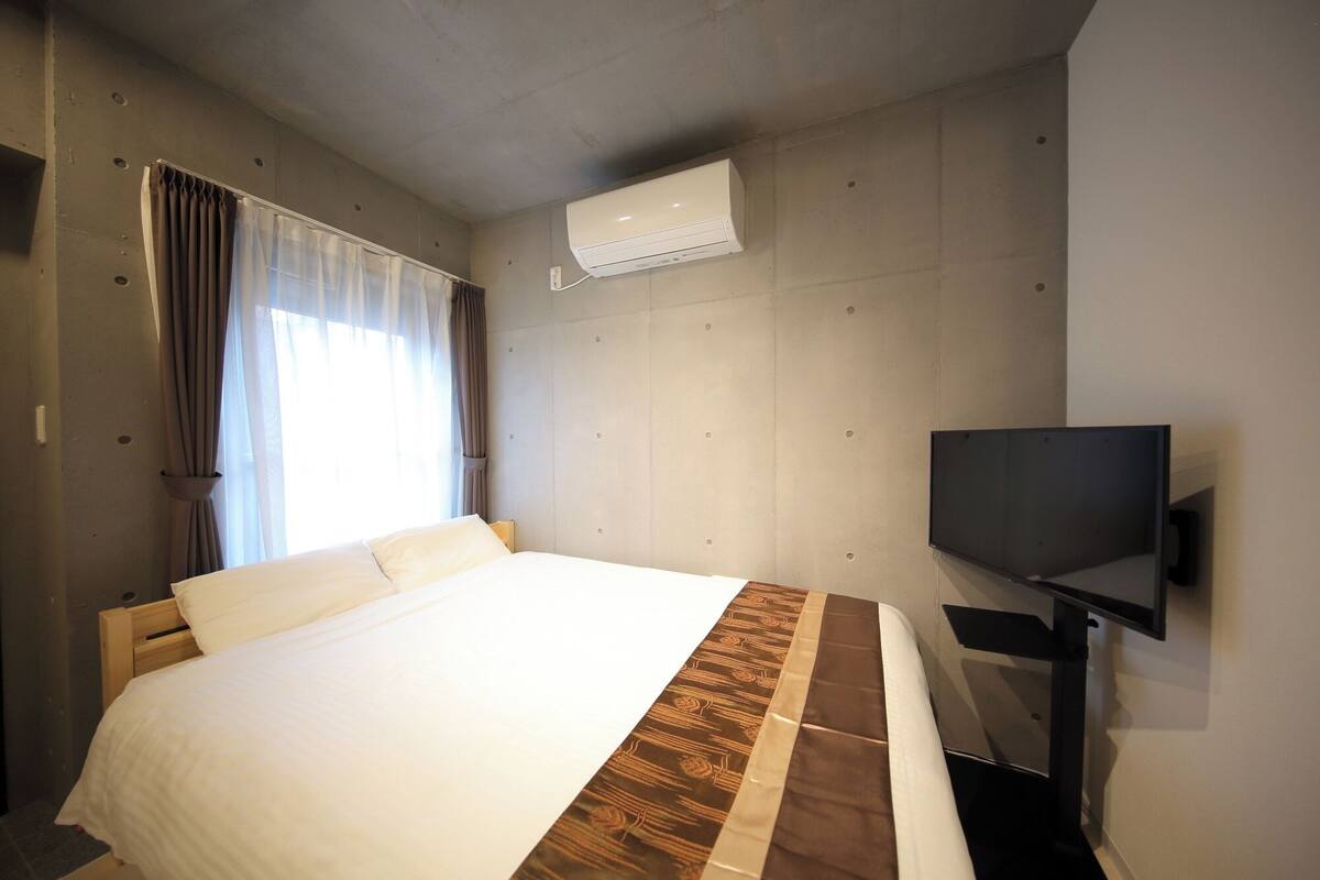 Ein Hotelzimmer mit Bett, Vorhängen, einer Klimaanlage und einem Fernseher.