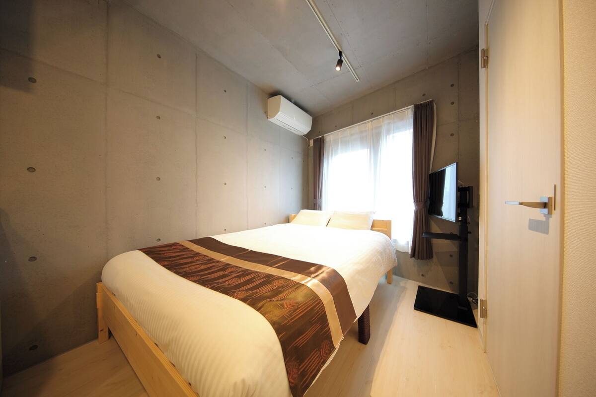 Ein Hotelzimmer mit einem großen Bett, einem Flachbildfernseher und einem Fenster mit Vorhängen.