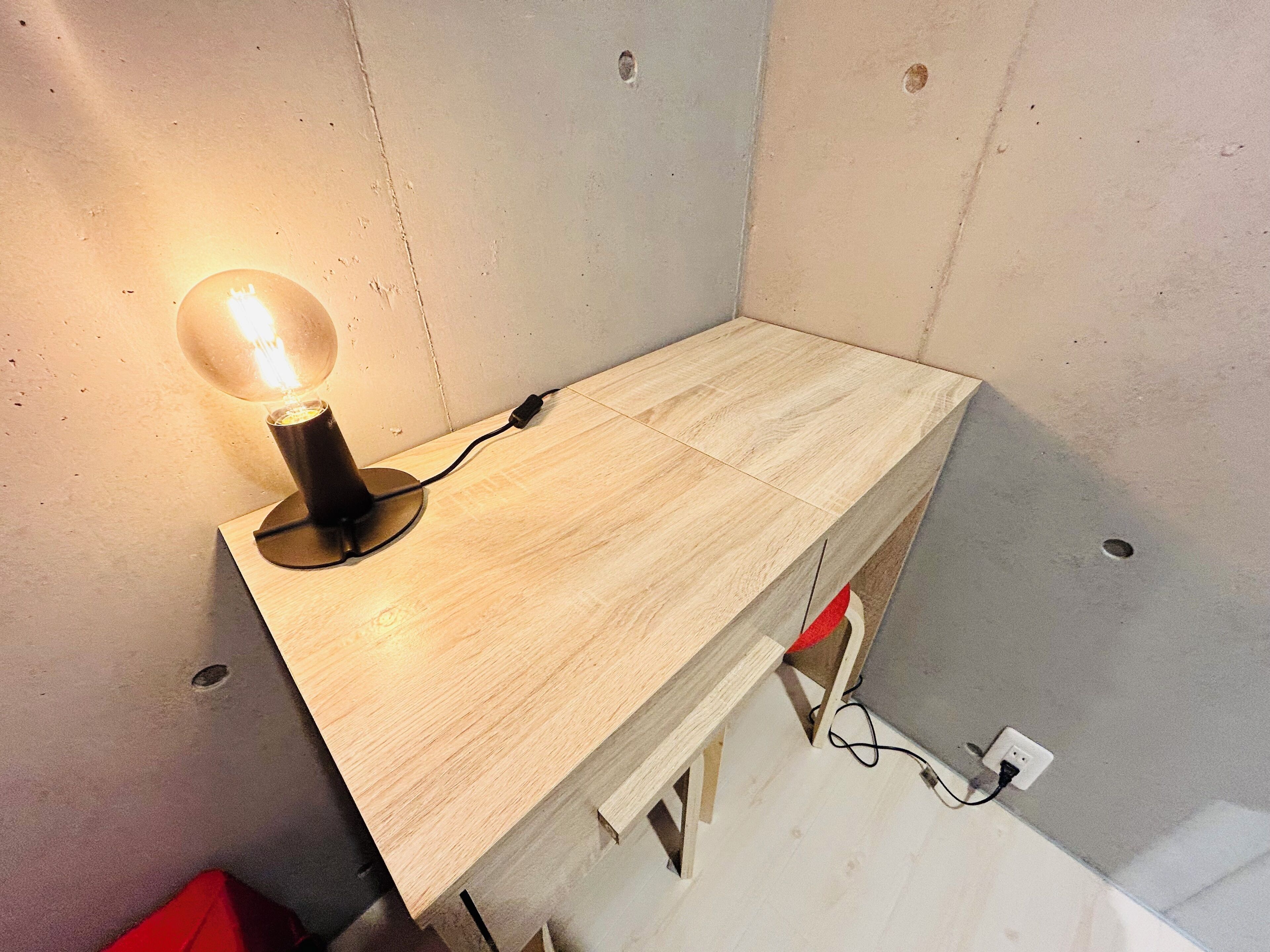 A wooden desk with a light bulb on it, connected to a power outlet.