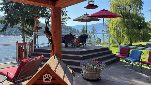 Un'area salotto esterna coperta con un pavimento in legno, una fioriera a forma di cuccia e vista su un lago e montagne.