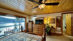Una camera da letto con un grande letto, soffitto in legno e vista su un lago.