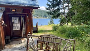 Un rustico chalet con facciata in legno, un cartello con il numero '289' e vista su un lago con un molo e una bandiera americana.