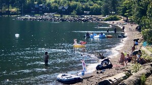 Una spiaggia sul lago con cigni gonfiabili, una barca e persone che si divertono in acqua.