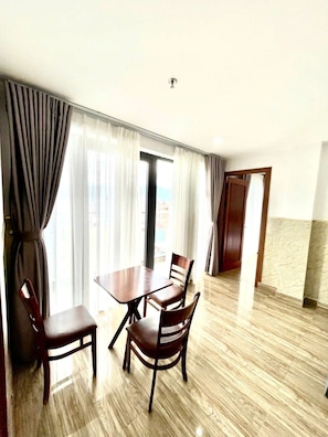 A hotel room with a dining table and chairs, a large window with curtains, a door, and a tiled floor. - Dong Kinh Hotel & Apartment (Da Nang)