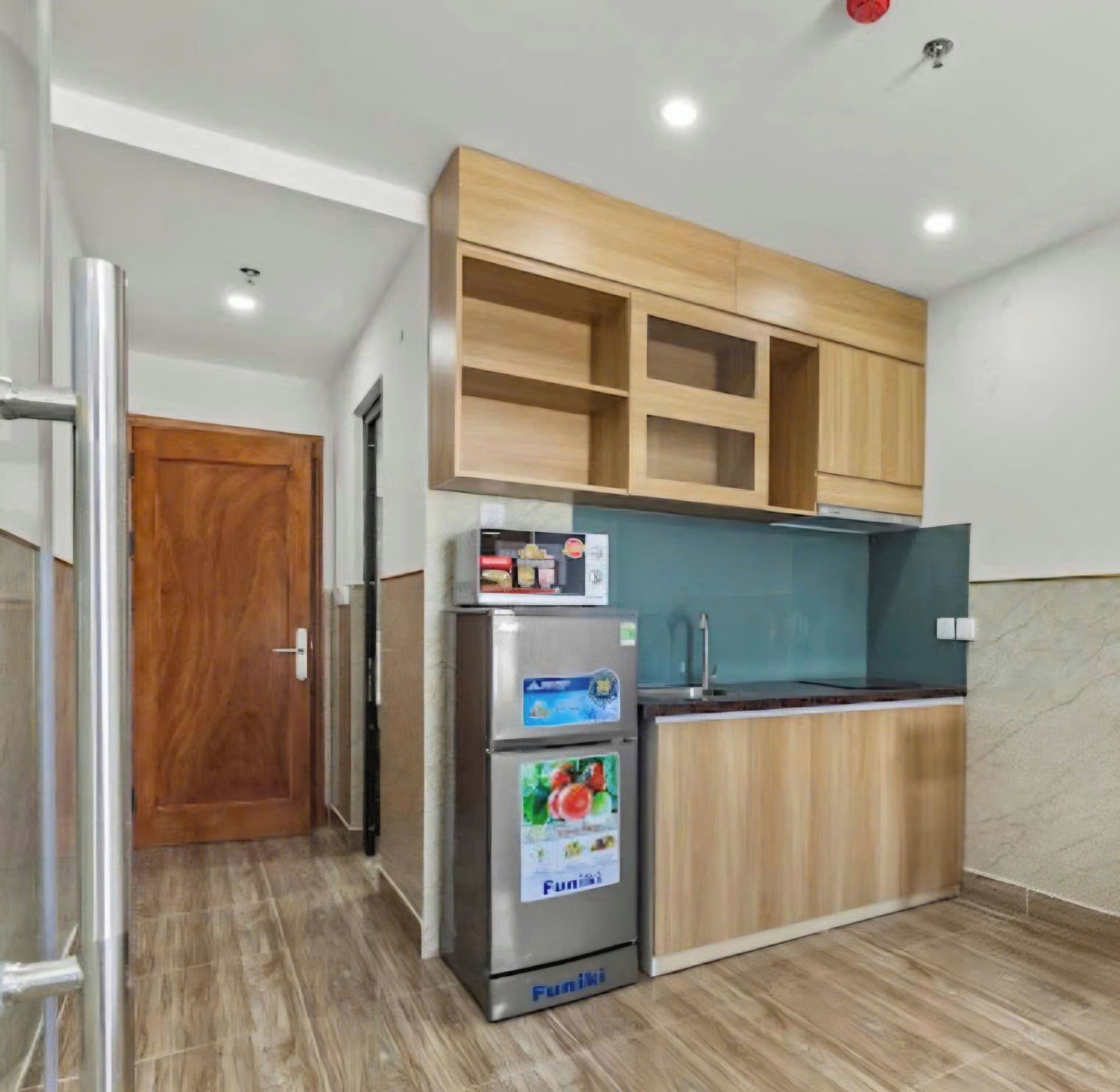A compact kitchen with a refrigerator, a microwave, and wooden cabinets.