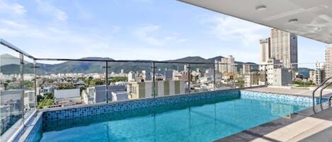 A rooftop pool with a city view, glass railings, and a clear sky.