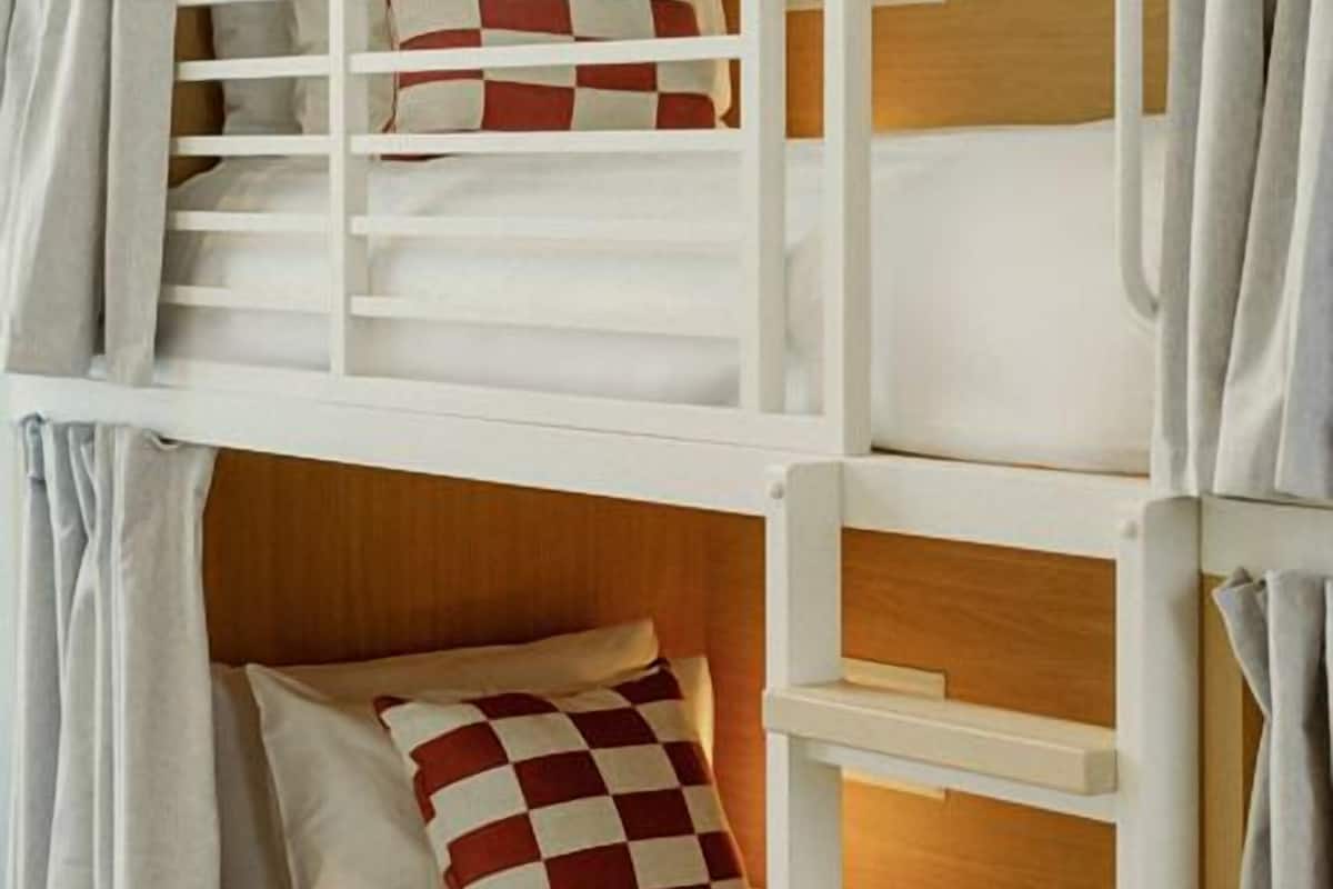 Una cama litera con cabecera de madera, una cama inferior con almohada de cuadros y una escalera.