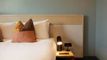 A neatly made bed with pillows, a bedside lamp, and a remote control on a wooden nightstand.