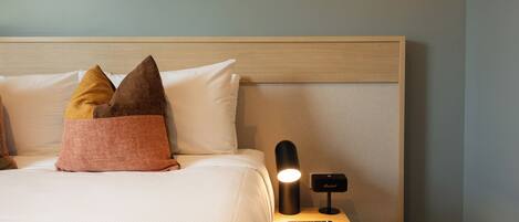 A neatly made bed with pillows, a bedside lamp, and a remote control on a wooden nightstand.