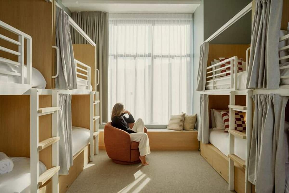 Una habitación con literas, un banco acolchado y un ventanal con cortinas.