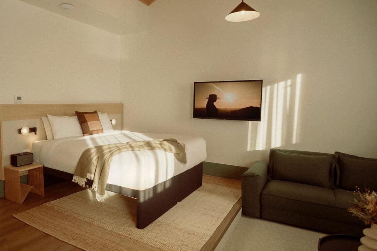 Un dormitorio con cama, mesita de noche, lámpara y un cuadro en la pared.
