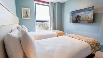 A hotel room with two beds, a large window, a mounted TV, and a framed picture on the wall.