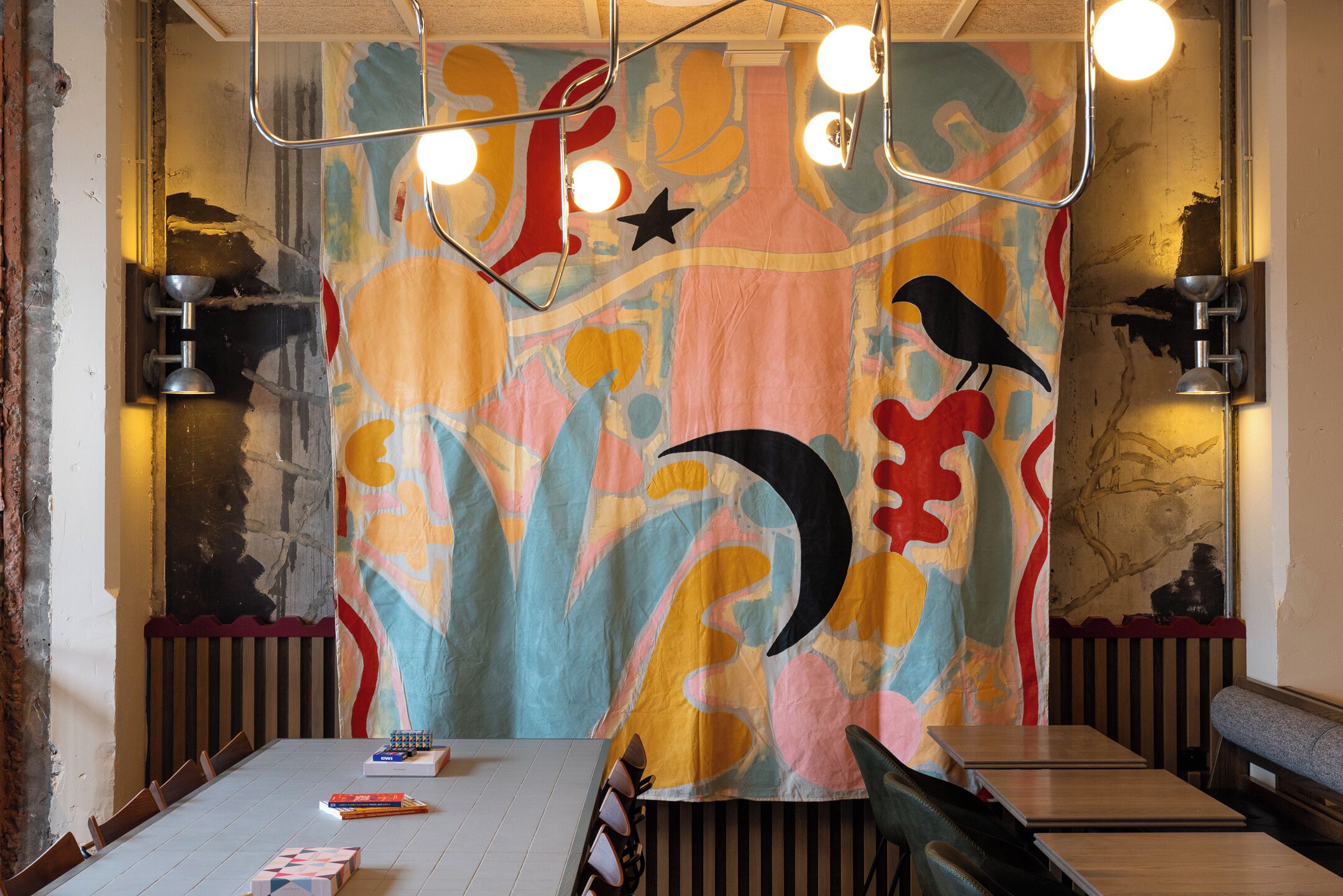 Un comedor con una mesa larga, sillas y un mural abstracto colorido en la pared.