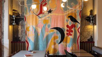 Un comedor con una mesa larga, sillas y un mural abstracto colorido en la pared.