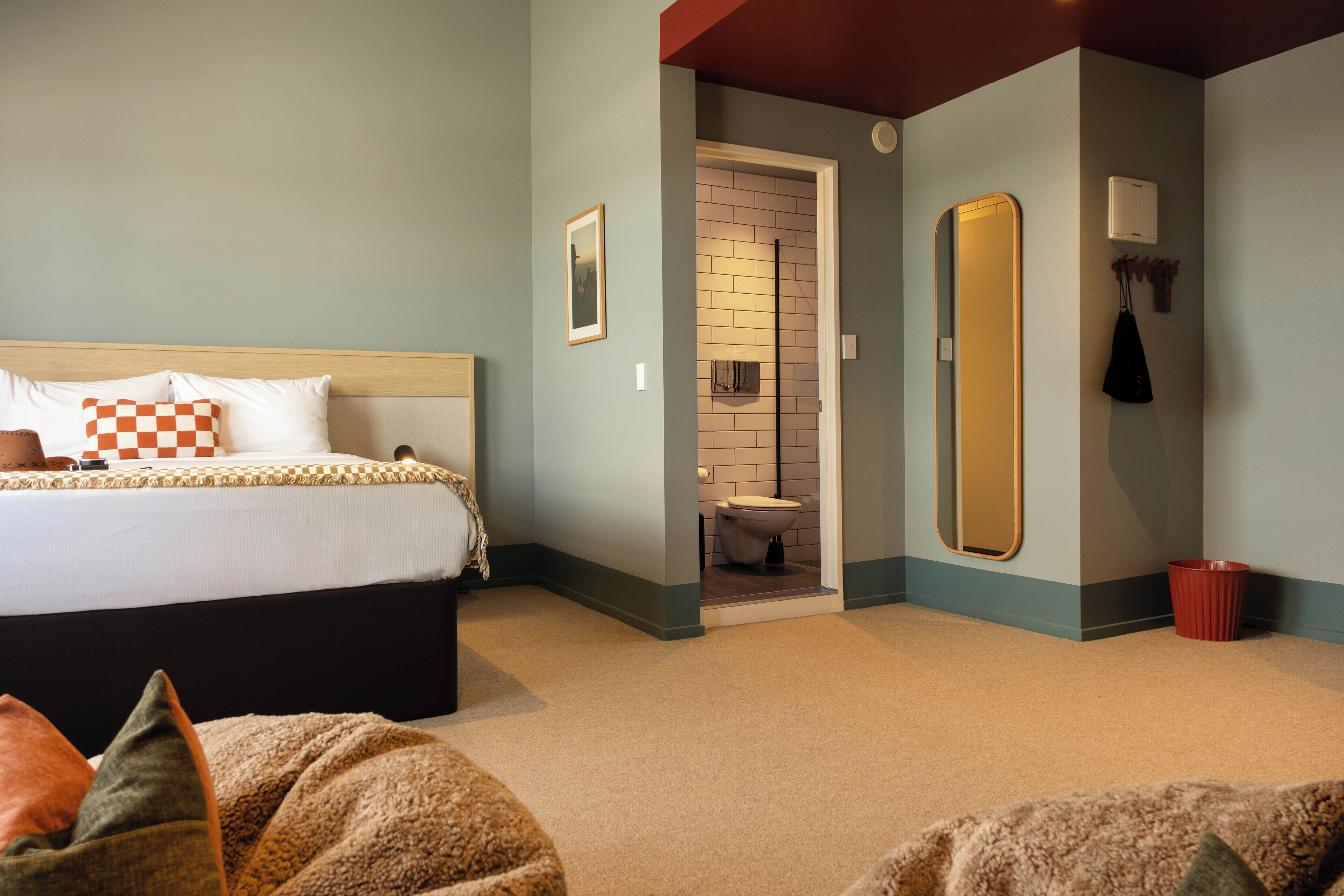 A bedroom with a bed, a bathroom with a toilet and a mirror, and a red trash bin.