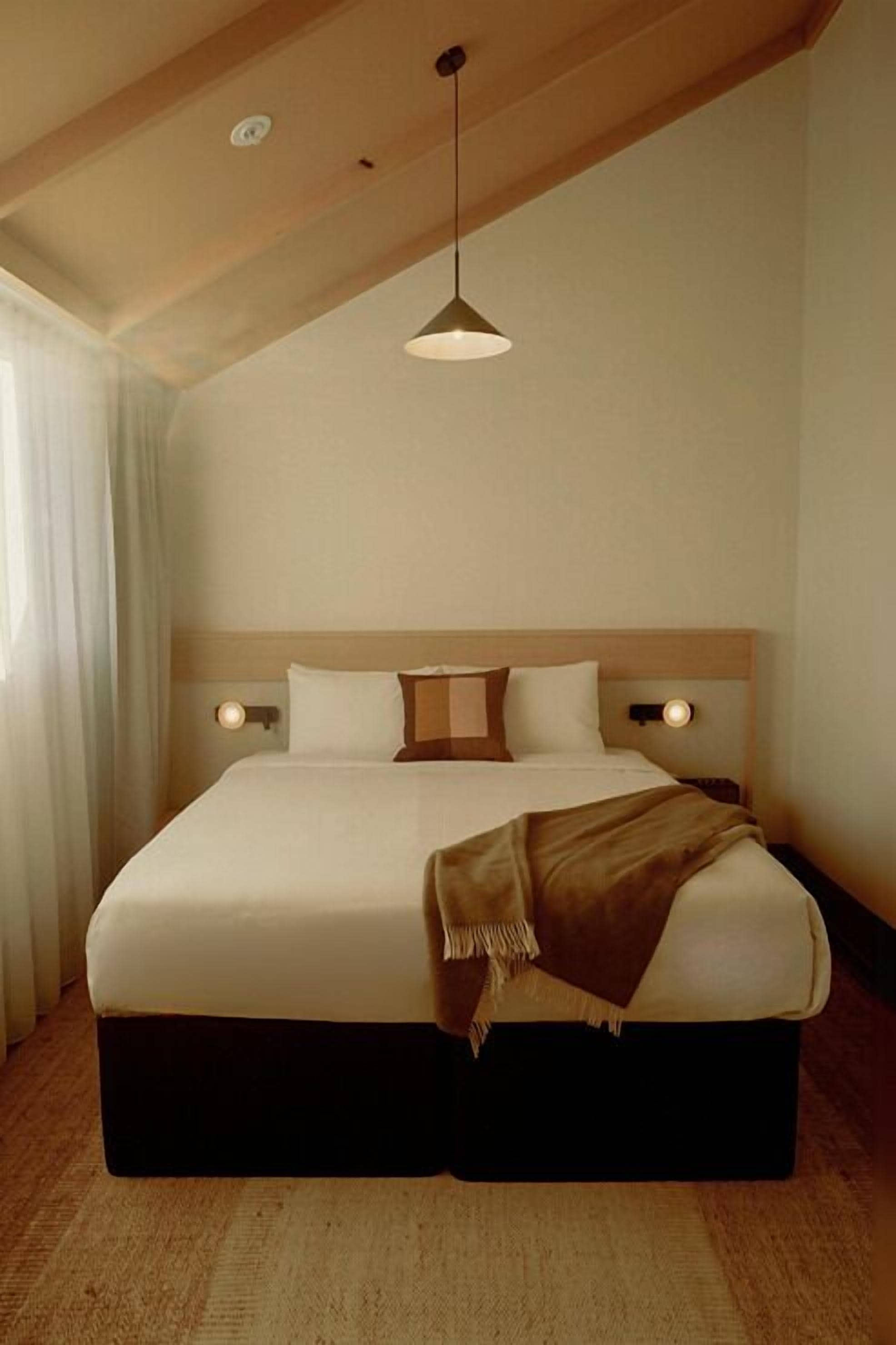 A neatly made bed with a wooden headboard, a hanging pendant light, and a bedside lamp.