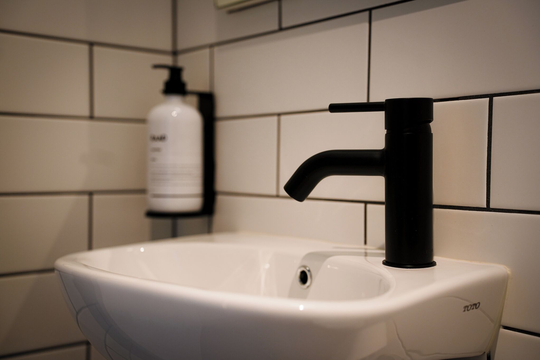 A bathroom sink with a black faucet and a bottle of hand soap in the background.