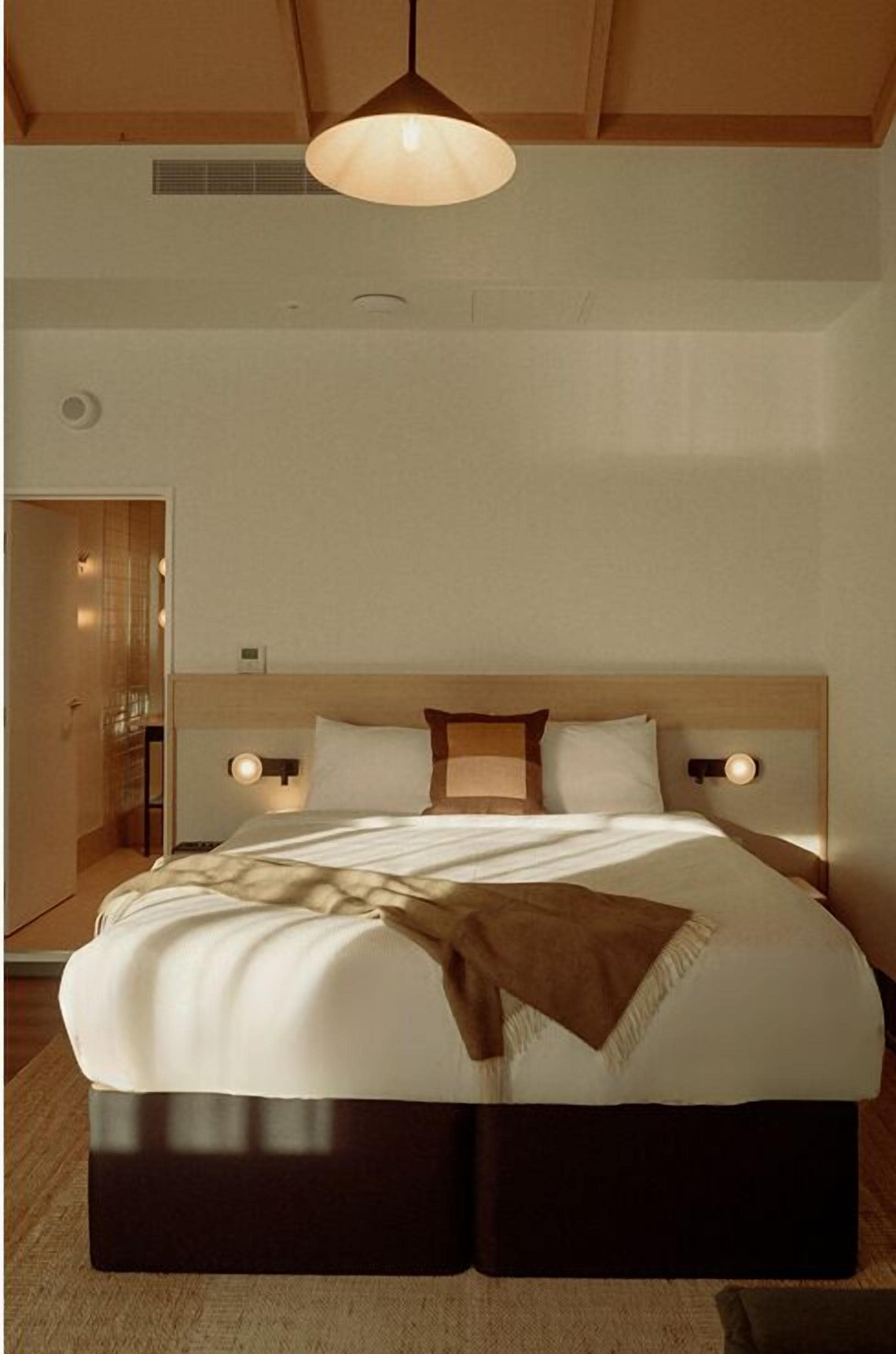 A large bed with a wooden headboard, two bedside lamps, and a hanging light fixture.