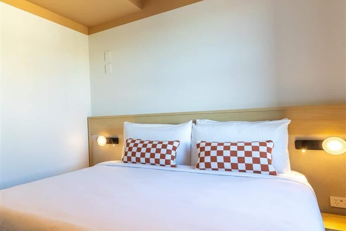 Habitación de hotel con cama, dos almohadas a cuadros y luces empotradas.