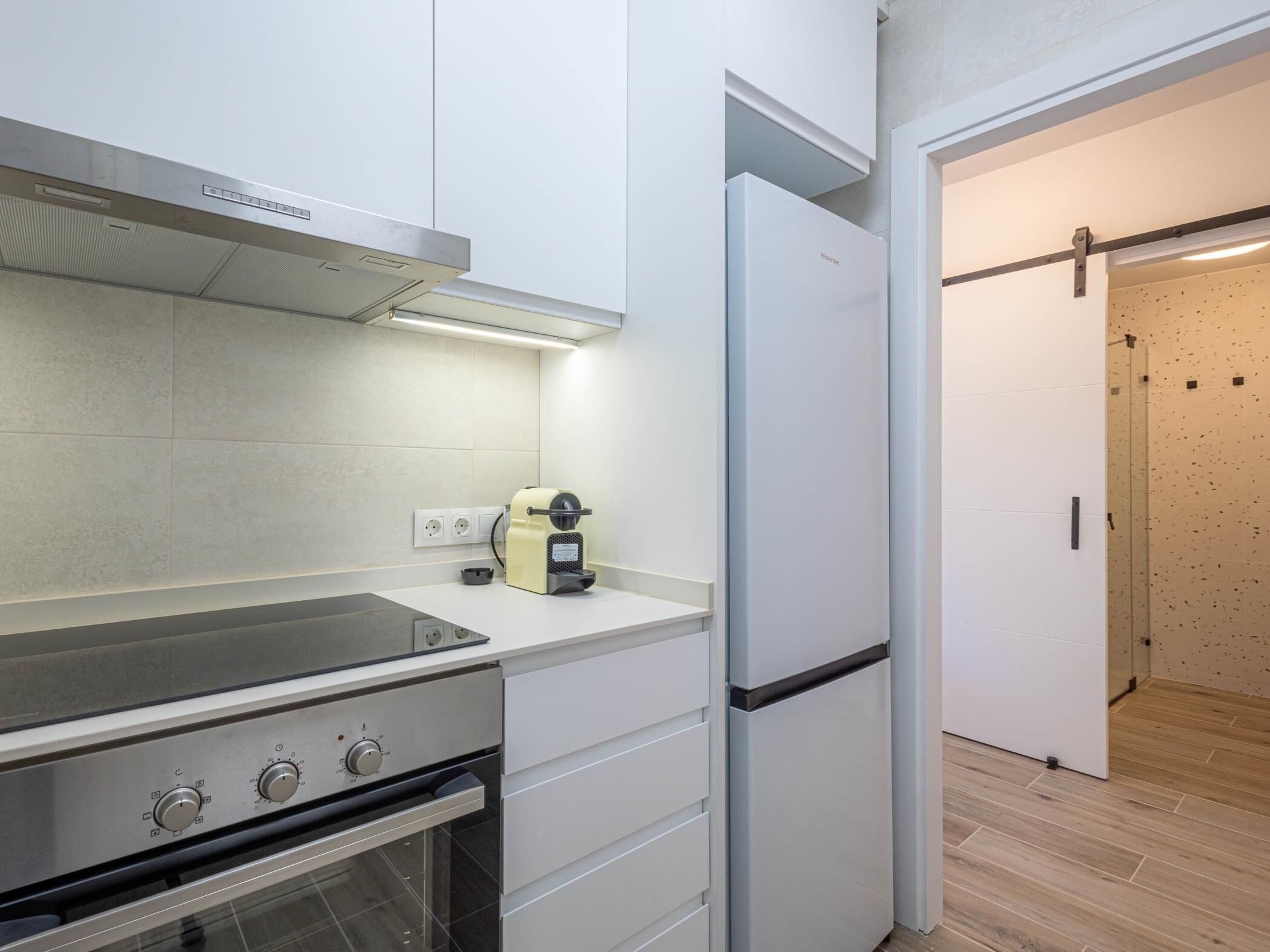 Una cocina moderna con horno empotrado, cafetera y refrigerador blanco.