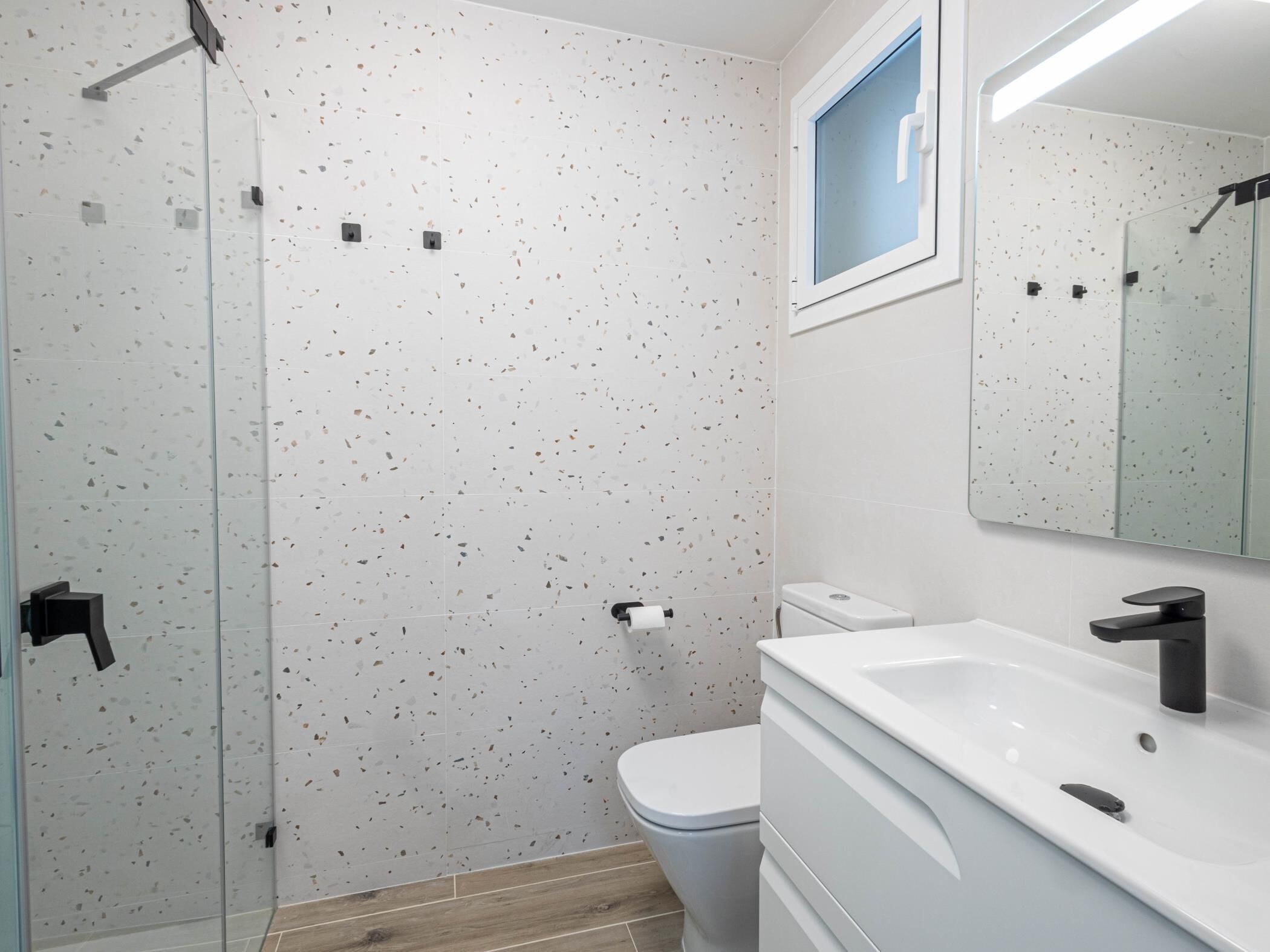 Une salle de bain moderne avec une douche à parois de verre, des toilettes et un lavabo avec un miroir au-dessus.