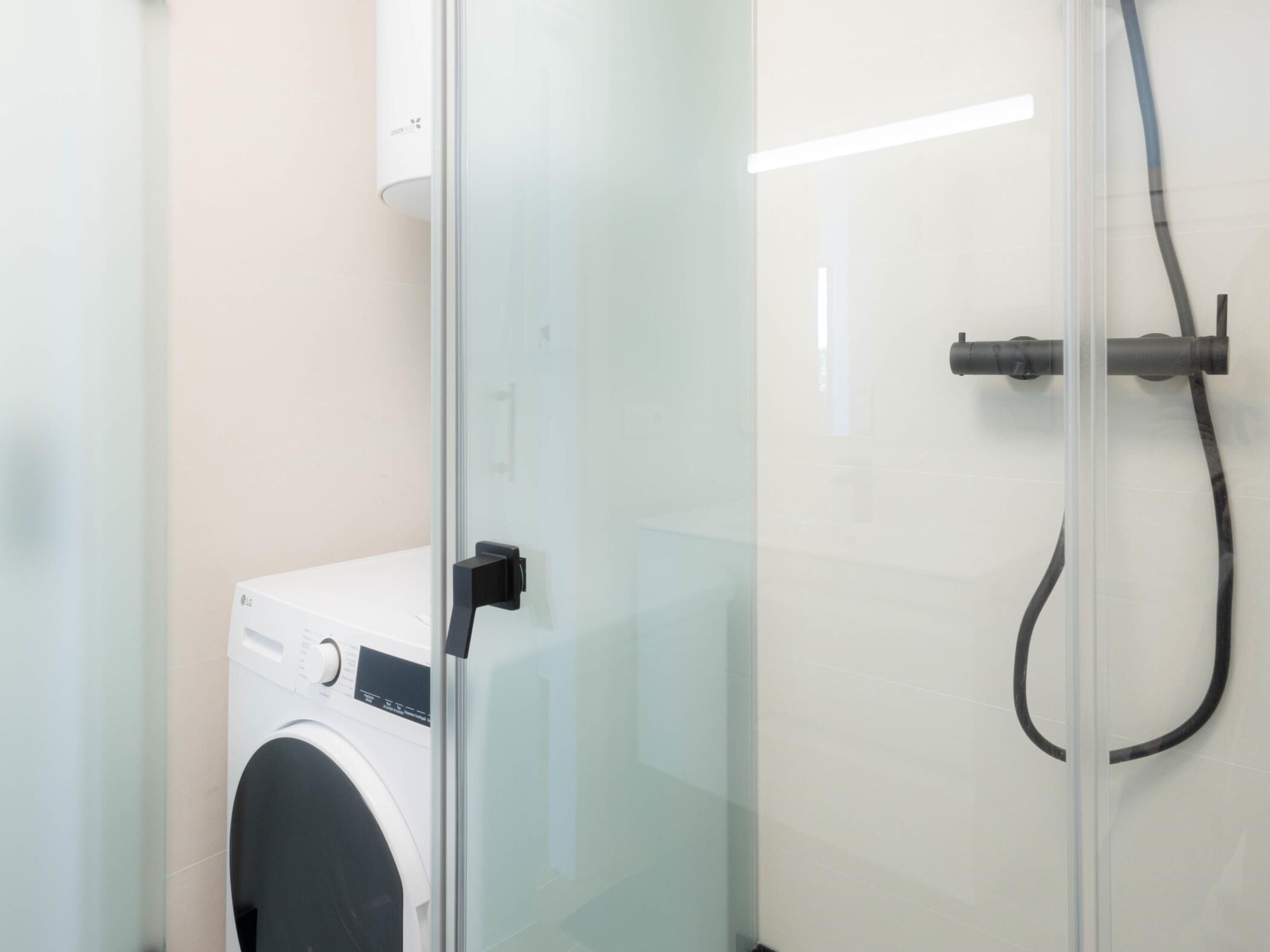 Ein kleines, modernes Badezimmer mit Duschkabine aus Glas, integrierter Waschmaschine und sichtbarem Wasseranschluss.