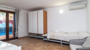 A bedroom with a bed, a sofa, a wardrobe, and a sliding glass door to a balcony. - Trilocale Baja Caddinas Dani (Golfo Aranci)