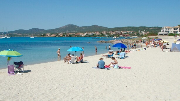 A beach with people sunbathing, umbrellas, and boats in the water. - Trilocale Baja Caddinas Dani (Golfo Aranci)