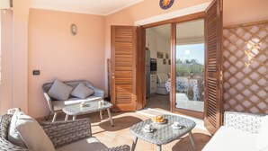 A balcony with wicker furniture, a table with a plate of food, and a view into the house. - Trilocale Baja Caddinas Dani (Golfo Aranci)