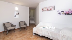A room with two wicker chairs, a white bed, and a staircase in the background. - Trilocale Baja Caddinas Dani (Golfo Aranci)