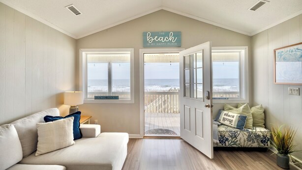 Una habitación con vista a la playa, un sofá con almohadones, una lámpara y un cartel que dice "The beach is my happy place".