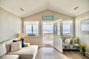A room with a view of the beach, a sofa with pillows, a lamp, and a sign that says "The beach is my happy place." - 4BD Oceanfront Beach Bungalow (Oak Island)
