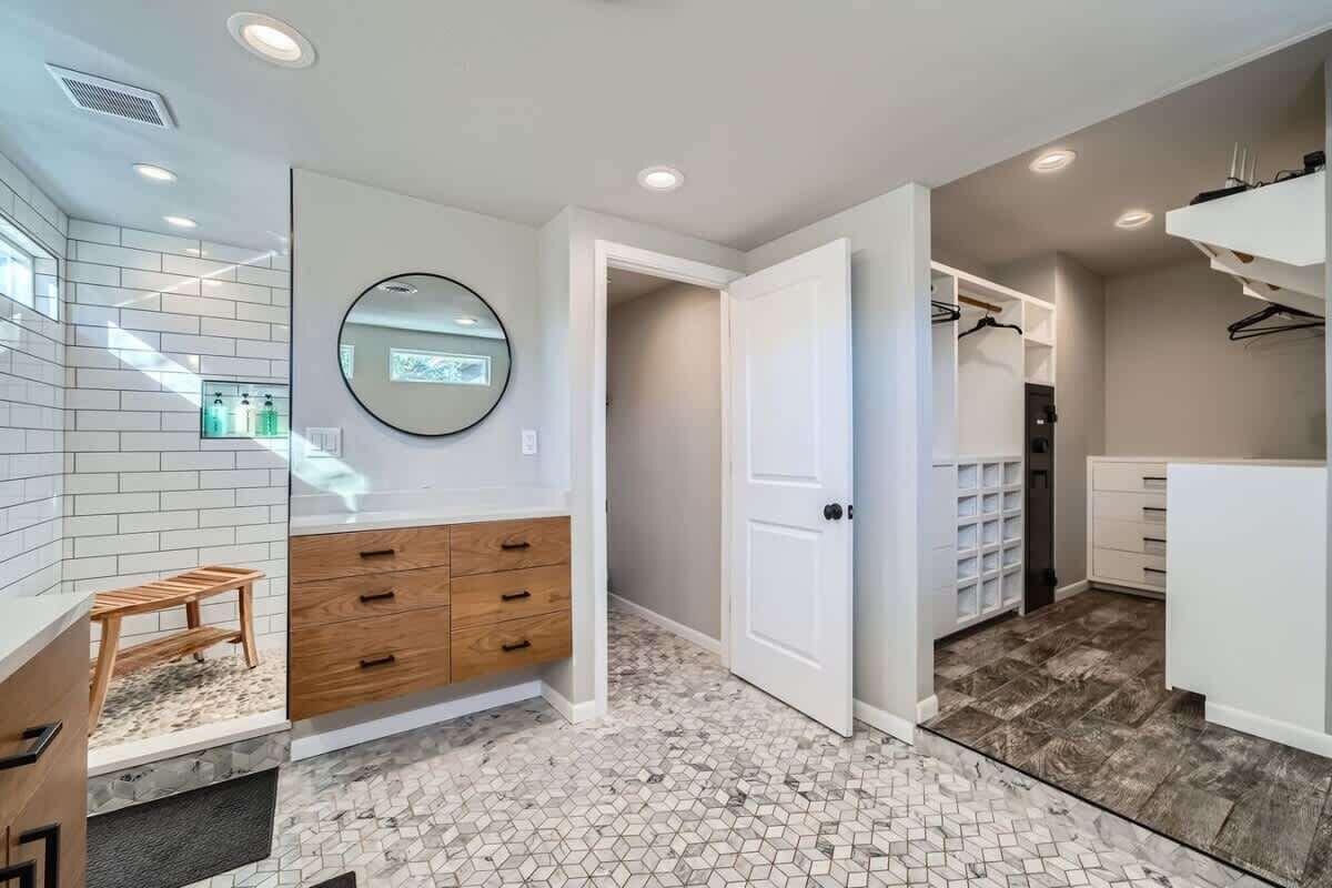A modern bathroom with a white vanity, wooden drawers, a round mirror, and a tiled floor.
