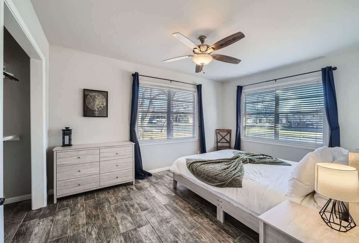 A bedroom with a bed, a ceiling fan, a dresser, and a window with curtains.