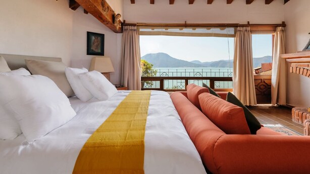 Habitación de hotel con una cama grande, vista al mar y balcón con baranda de madera.