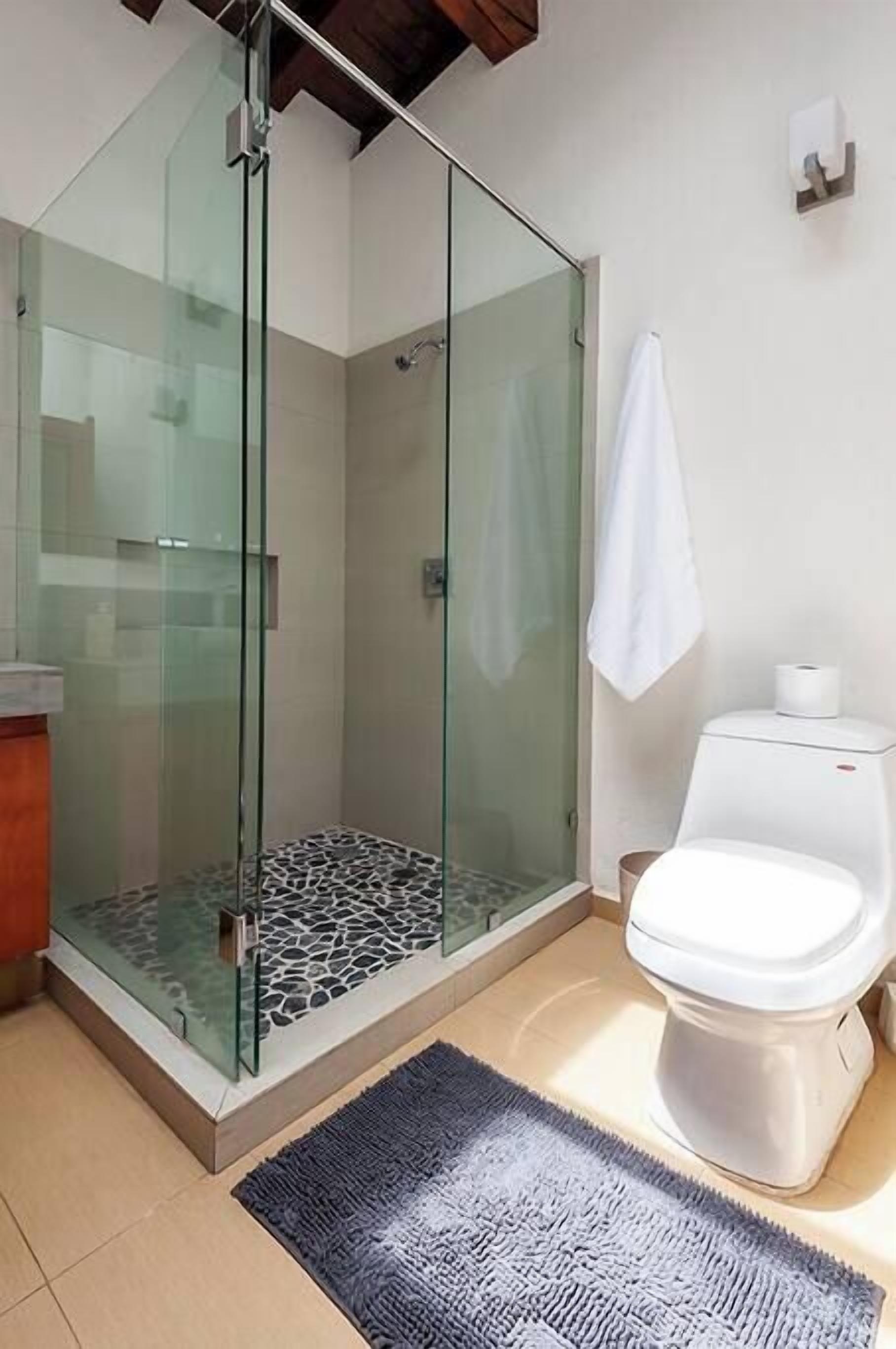 Ein modernes Badezimmer mit einer gläsernen Dusche, einer weißen Toilette und einem strukturierten Boden.