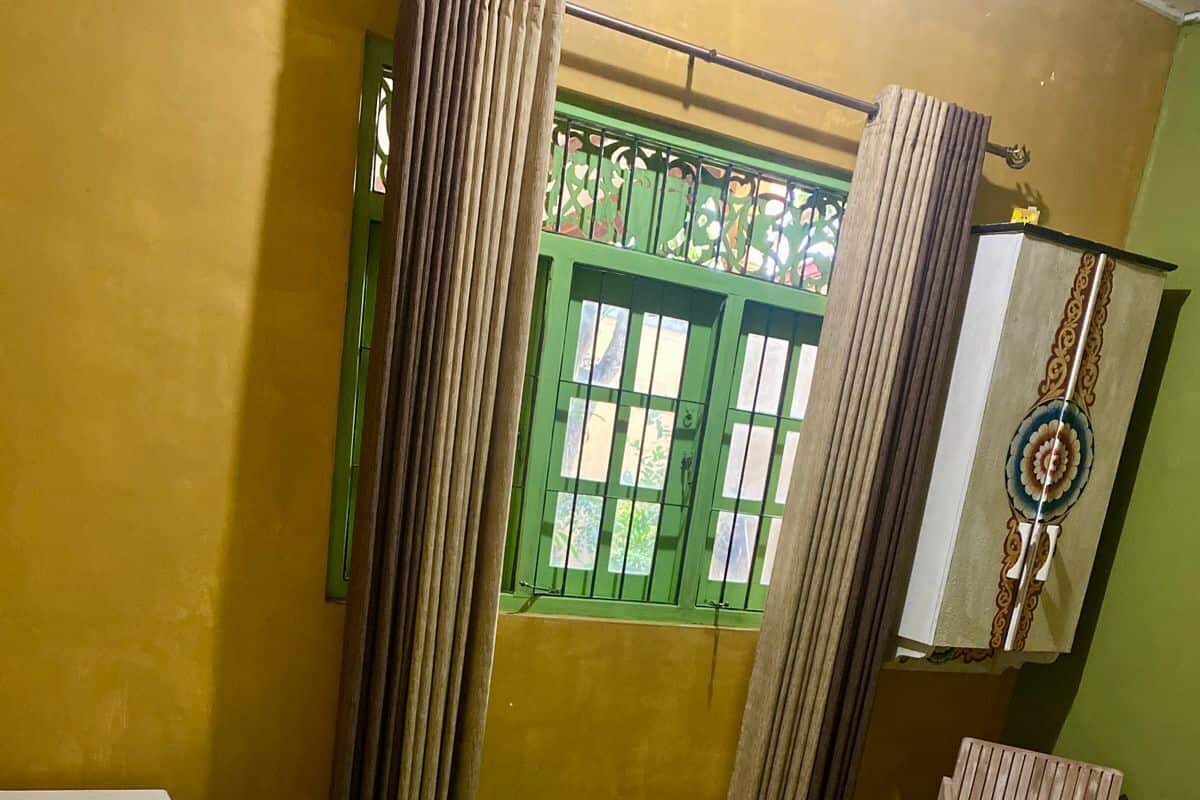 A single-bed room with a green bedspread, white pillows, and a green curtain.