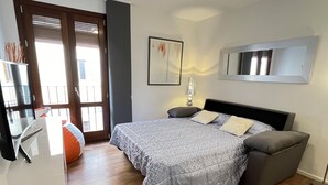 Une chambre à coucher avec un lit, des tables de chevet, une lampe, un miroir et une porte-fenêtre donnant sur un balcon.