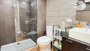 Une salle de bain moderne avec une douche à parois de verre, des toilettes blanches et un meuble-lavabo doté d’un miroir et d’un évier.