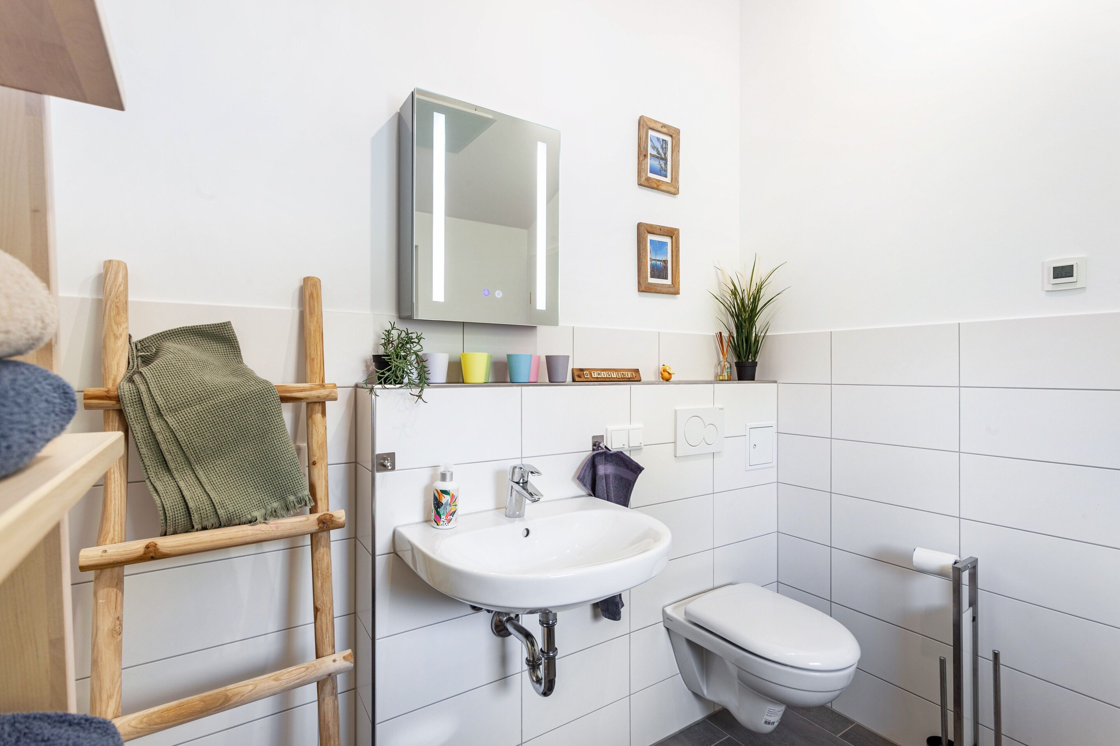Ein Badezimmer mit weißem Waschbecken, Toilette, einer Holzleiter, einem Spiegel und einem Ablagebereich mit Pflegeprodukten.