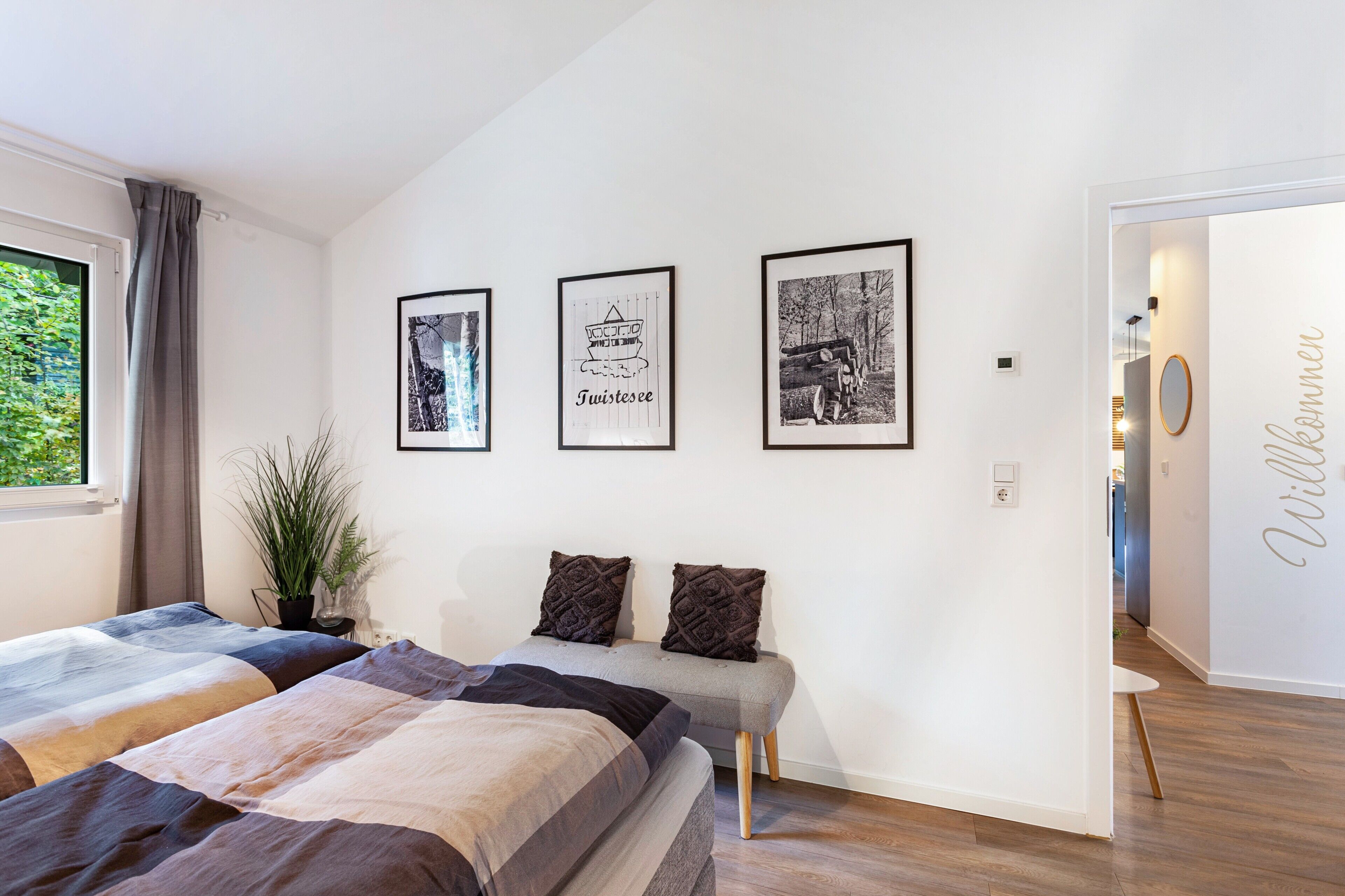 Ein modernes Schlafzimmer mit zwei Betten, einer Bank und drei gerahmten Bildern an der Wand.
