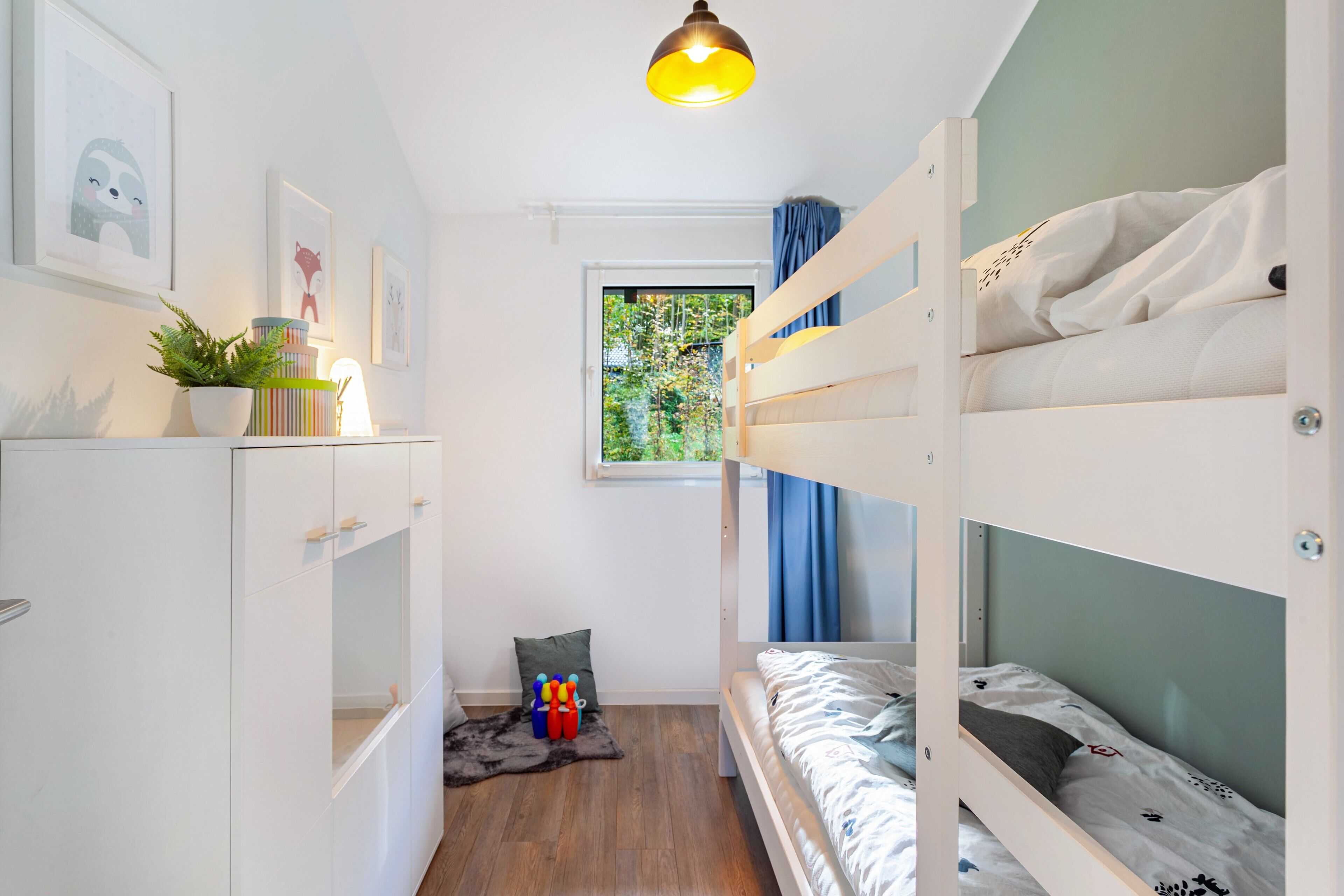 Habitación con literas, una ventana, una planta y una estantería con libros y una lámpara.